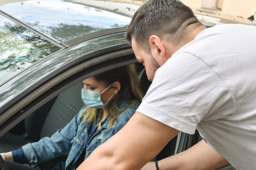 Woman in a car with a face mask and a man showing her how to drive