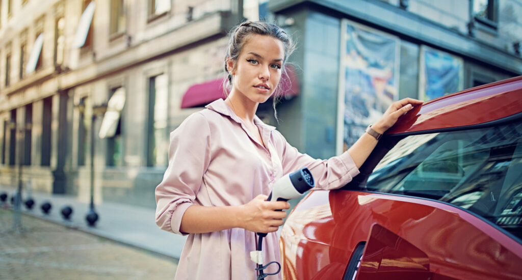 Portrait of young girl charging her electric car in the city