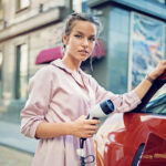 Portrait of young girl charging her electric car in the city