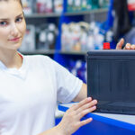 Beautiful girl saleswoman offers the best battery for car in an auto parts store