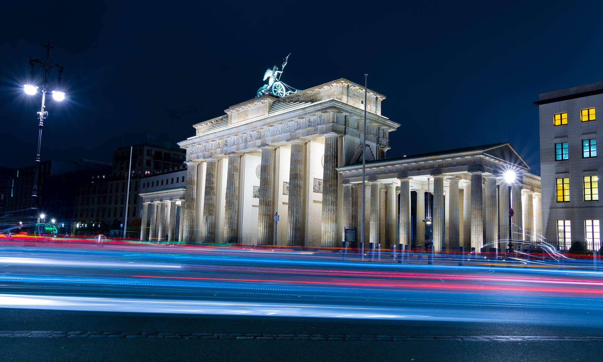 Berlin Brandenburg Gate at night time with color streak from passing vehicle showing contrast between motion vs permanence