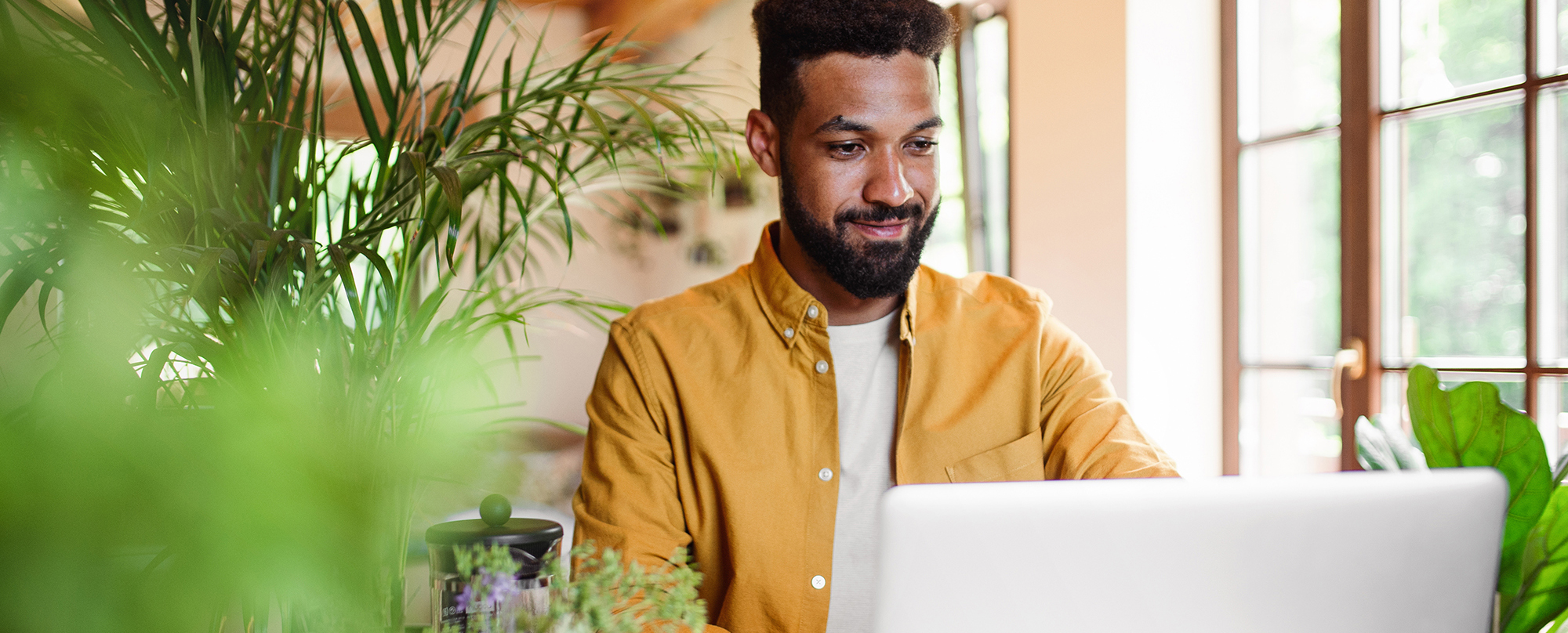 Young man with laptop and coffee working indoors, home office concept.