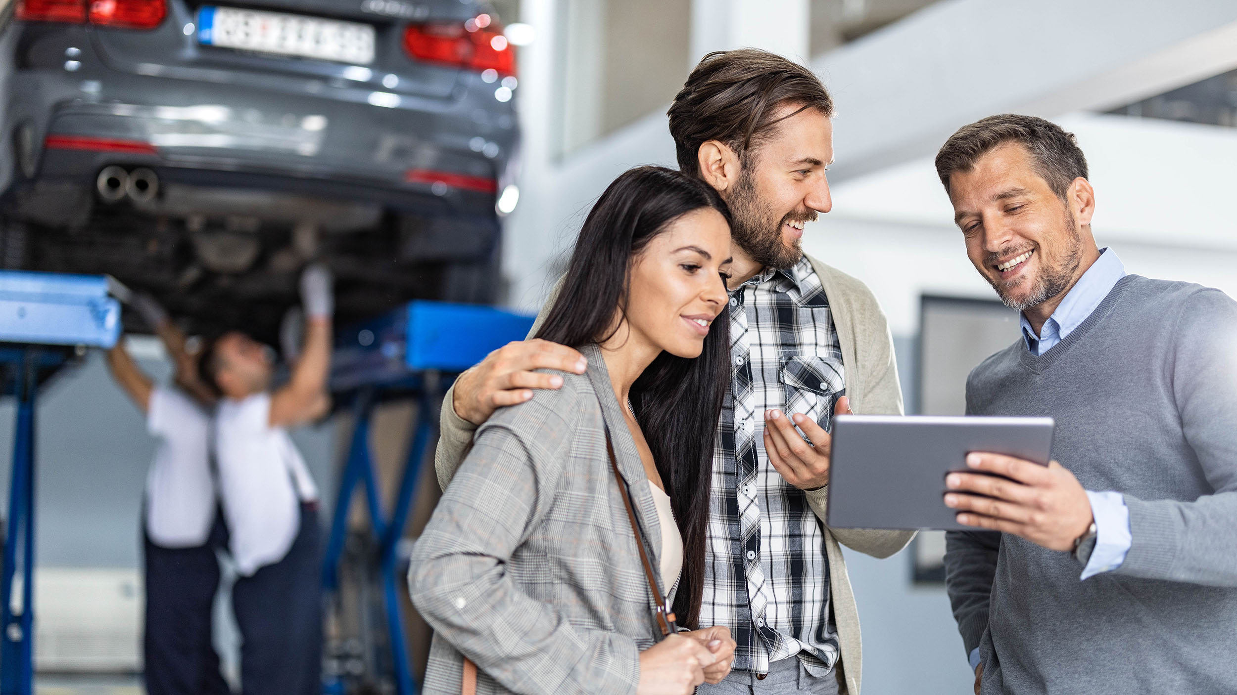 Happy manager and young couple using touchpad in auto repair shop.