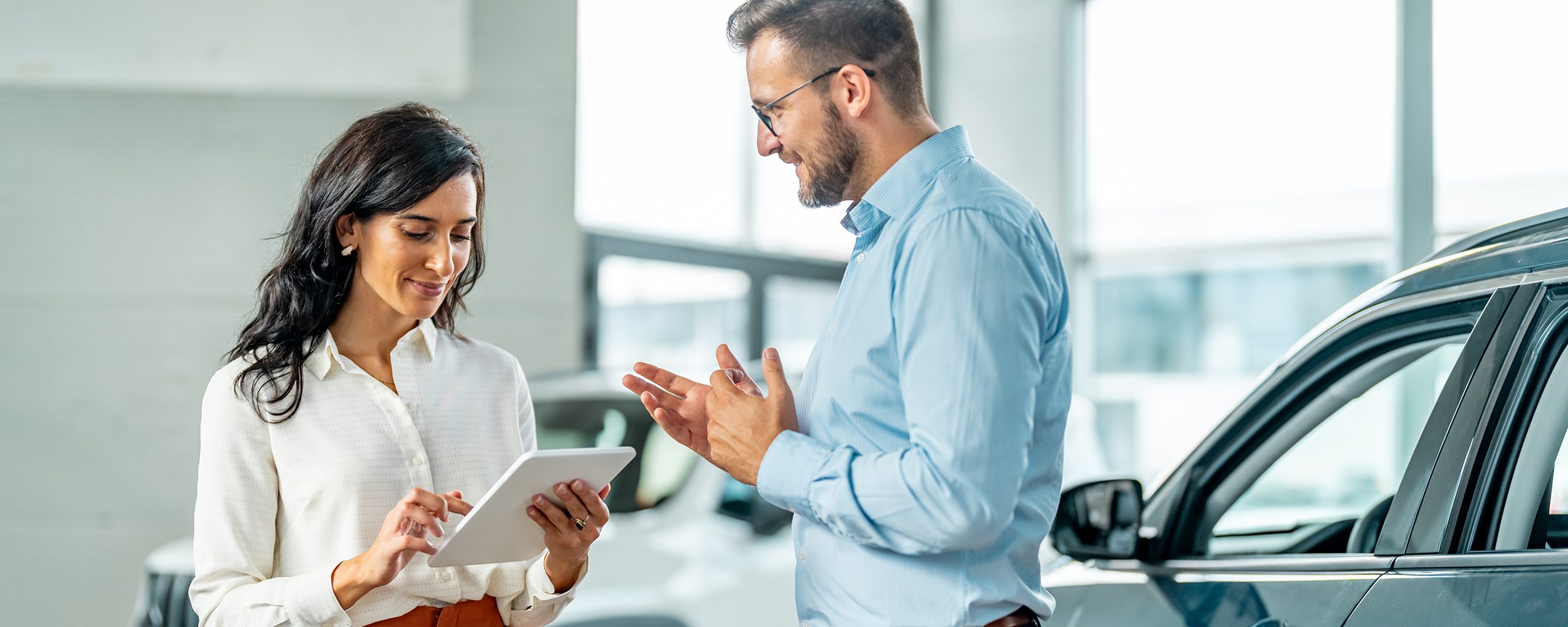 Cheerful car dealership customer talking to auto sales consultant