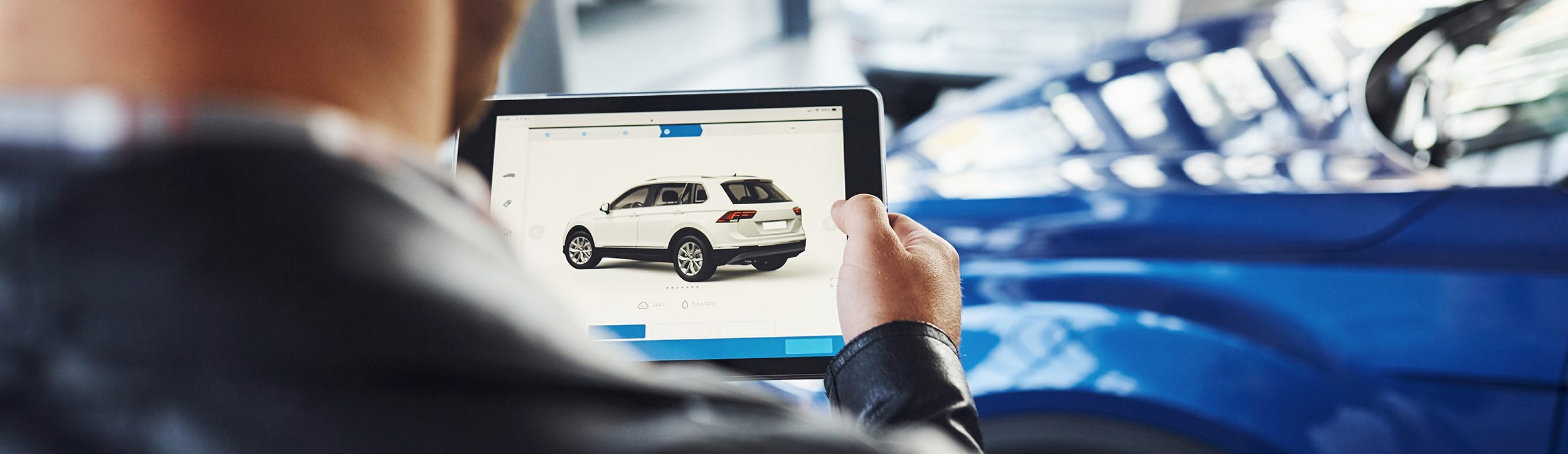 Man stands inside car salon with tablet in hands and looks at the vehicle picture
