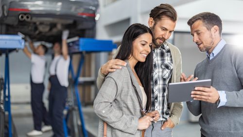 Mid adult manager and young couple using touchpad in auto repair shop.